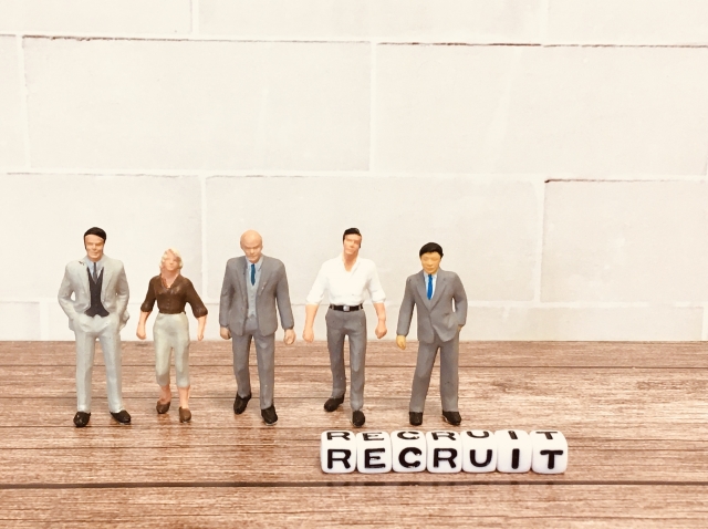 スーツ姿のビジネスパーソンのミニチュアフィギュアと「RECRUIT（採用）」と書かれたブロック。外資系企業における中途採用・人材募集のイメージ